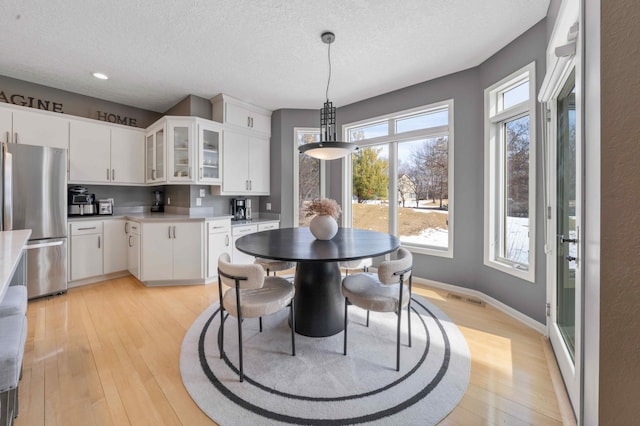 dining space with visible vents, baseboards, a textured ceiling, and light wood-style flooring