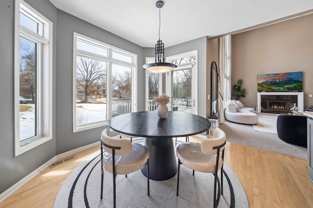 dining space featuring visible vents, baseboards, a lit fireplace, light wood-style floors, and a textured ceiling