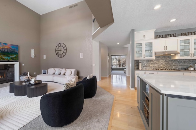 living room with visible vents, light wood finished floors, a high ceiling, recessed lighting, and a glass covered fireplace