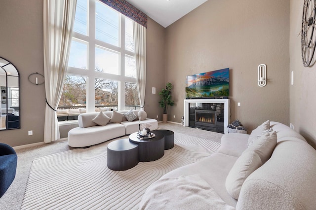 carpeted living area featuring a tile fireplace, baseboards, and a towering ceiling