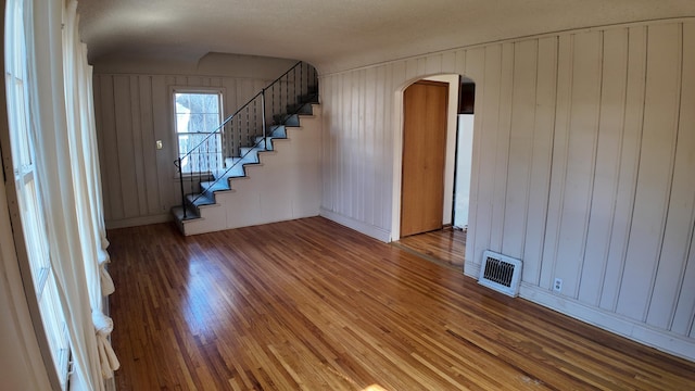 interior space featuring arched walkways, visible vents, stairway, and wood finished floors