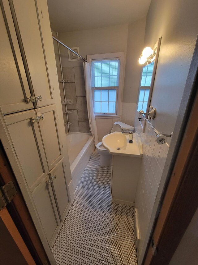 full bathroom with shower / bathtub combination with curtain, toilet, tile walls, wainscoting, and vanity