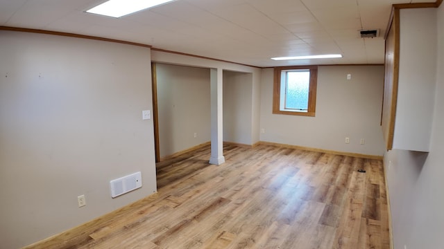 basement with ornamental molding, wood finished floors, visible vents, and baseboards