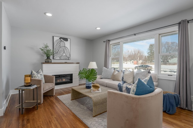 living area with a glass covered fireplace, baseboards, wood finished floors, and recessed lighting