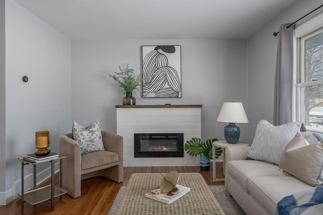 living room with a glass covered fireplace, wood finished floors, visible vents, and baseboards