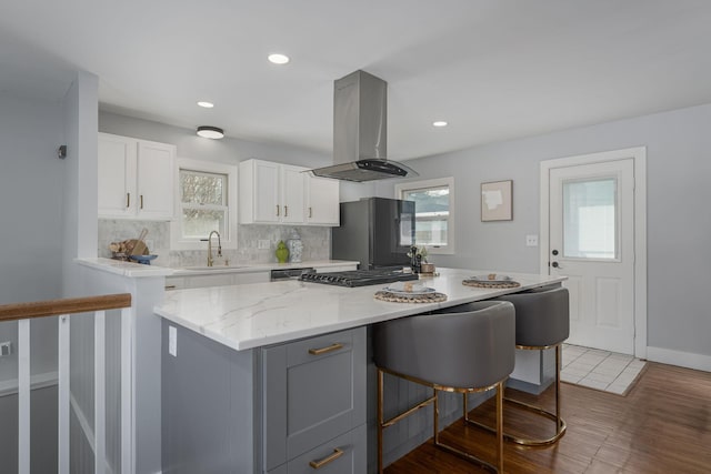 kitchen featuring freestanding refrigerator, a sink, decorative backsplash, white cabinetry, and island range hood