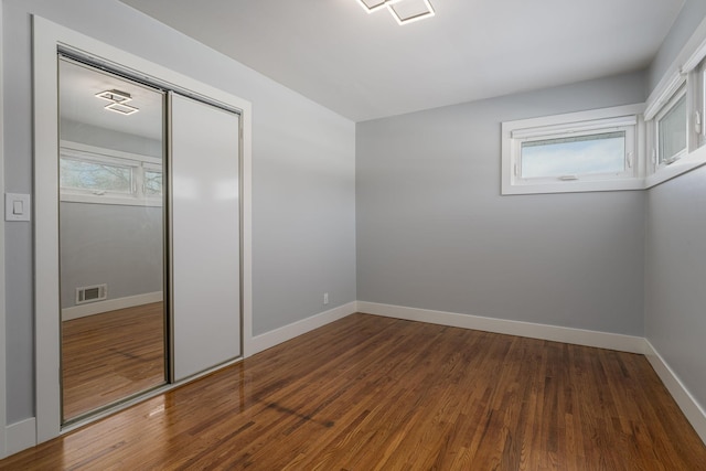 unfurnished bedroom with wood finished floors, visible vents, a closet, and baseboards