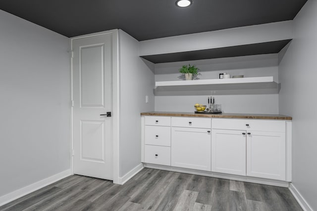 bar featuring a bar, baseboards, and dark wood-style flooring