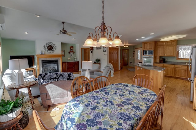 dining room with recessed lighting, light wood-style flooring, a tile fireplace, and vaulted ceiling