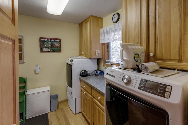 washroom with light wood-style flooring, a textured ceiling, cabinet space, separate washer and dryer, and baseboards