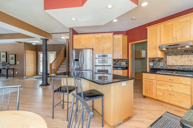 kitchen with under cabinet range hood, a kitchen bar, appliances with stainless steel finishes, and light wood finished floors