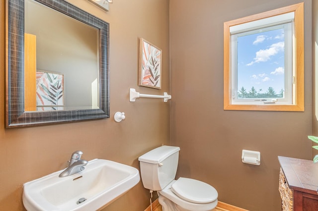 half bathroom featuring toilet, baseboards, and a sink