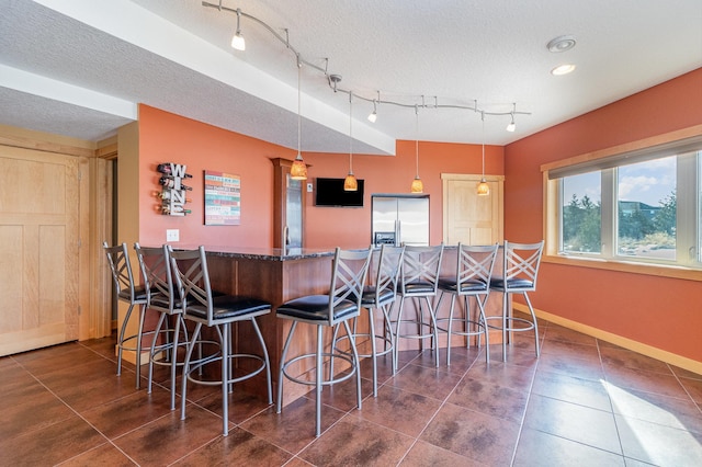 kitchen with a textured ceiling, baseboards, stainless steel refrigerator with ice dispenser, pendant lighting, and a kitchen breakfast bar