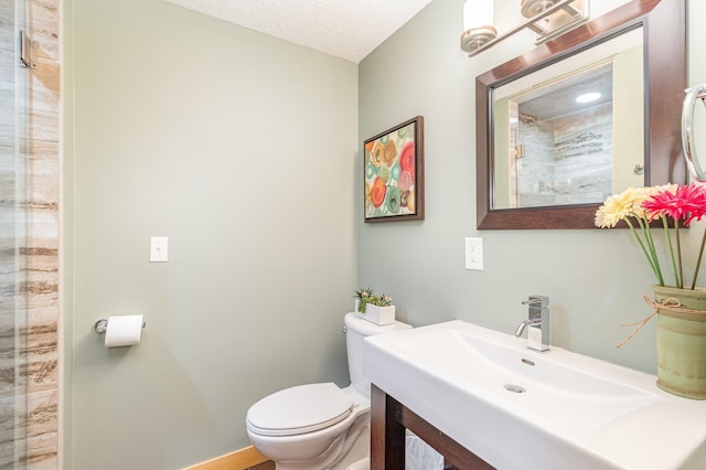 bathroom with a textured ceiling, toilet, vanity, and baseboards