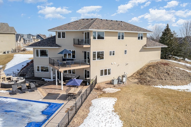 rear view of house with stucco siding, a patio, fence, a balcony, and stairs