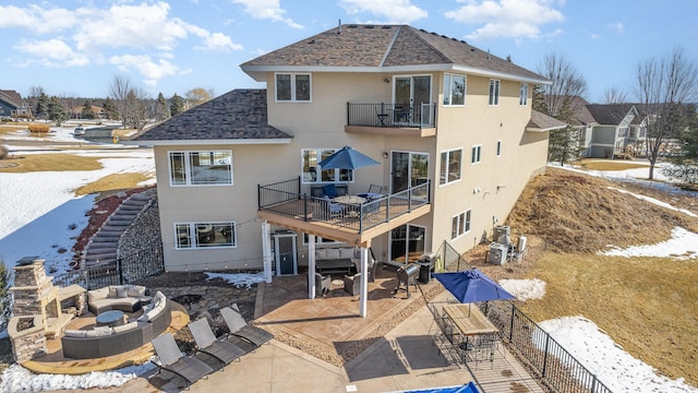 snow covered property with stucco siding, a patio, a fenced backyard, a fire pit, and a balcony