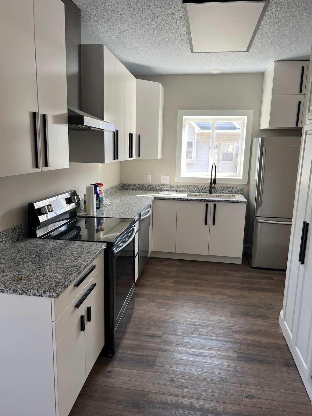 kitchen featuring a sink, stone counters, appliances with stainless steel finishes, wall chimney exhaust hood, and dark wood-style flooring