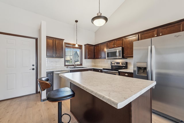 kitchen with a sink, dark brown cabinetry, light countertops, appliances with stainless steel finishes, and a center island