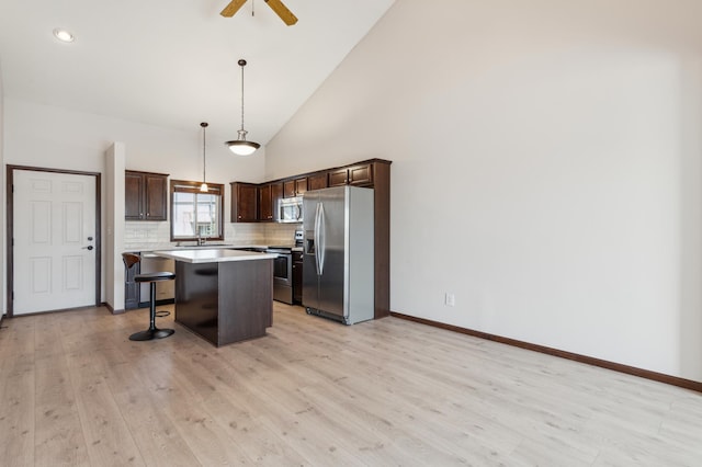 kitchen with light wood-style flooring, a kitchen breakfast bar, dark brown cabinetry, appliances with stainless steel finishes, and light countertops