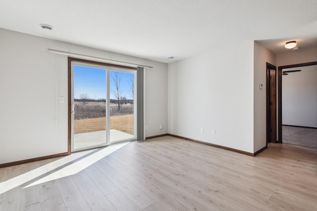 unfurnished room with baseboards, a textured ceiling, and light wood-style flooring