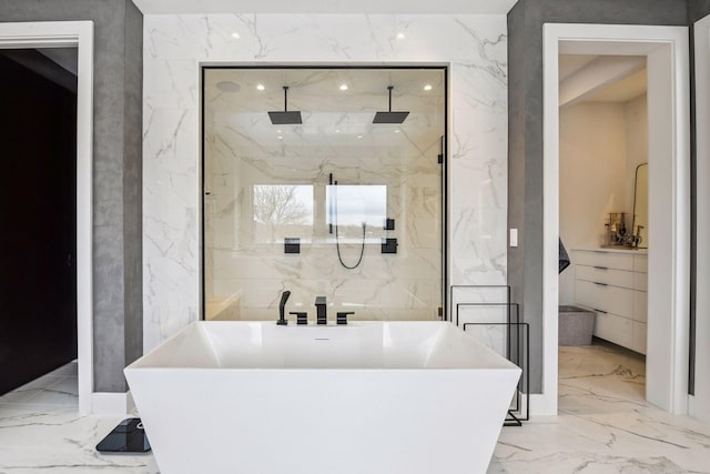 full bath featuring marble finish floor, stone wall, and a freestanding tub