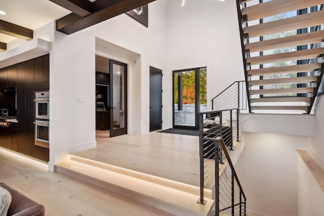 foyer entrance with beam ceiling, a high ceiling, wood finished floors, and stairs