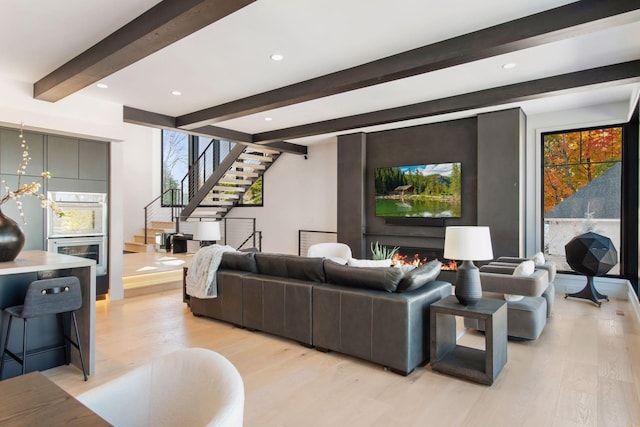 living area with recessed lighting, a warm lit fireplace, stairs, light wood-style floors, and beamed ceiling