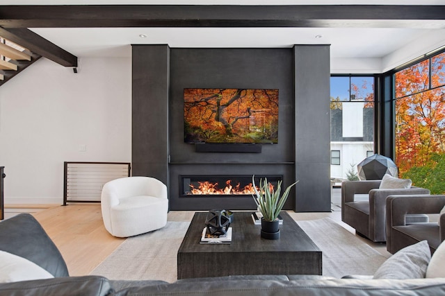 living room featuring stairway, wood finished floors, baseboards, lofted ceiling with beams, and a glass covered fireplace