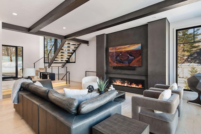 living room with light wood-type flooring, beamed ceiling, plenty of natural light, a fireplace, and stairs