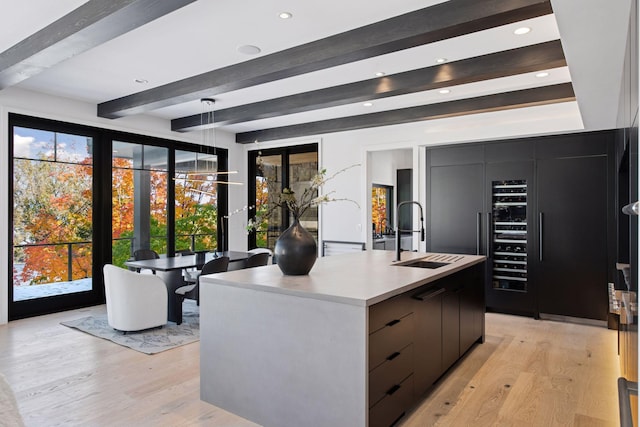 kitchen with light wood finished floors, modern cabinets, a center island with sink, a sink, and light countertops