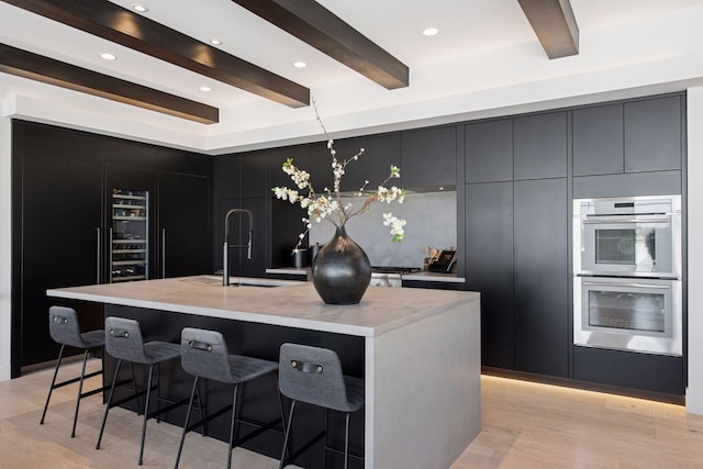 kitchen featuring a breakfast bar, light wood-type flooring, stainless steel double oven, modern cabinets, and a sink