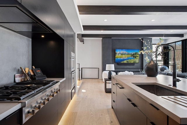 kitchen with beam ceiling, stainless steel gas stovetop, modern cabinets, and light wood finished floors