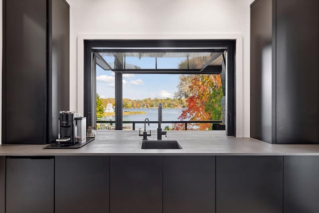 kitchen with a sink, a water view, modern cabinets, and light countertops