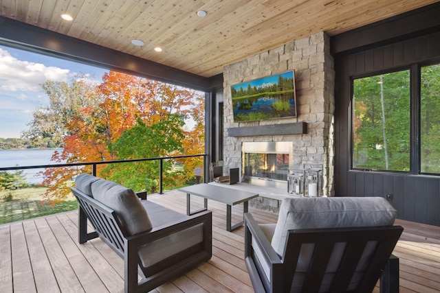 wooden terrace with an outdoor living space with a fireplace and a water view