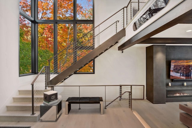 staircase with a glass covered fireplace, a high ceiling, and wood finished floors