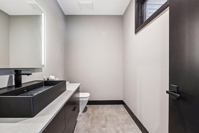 half bathroom featuring visible vents, baseboards, toilet, and vanity