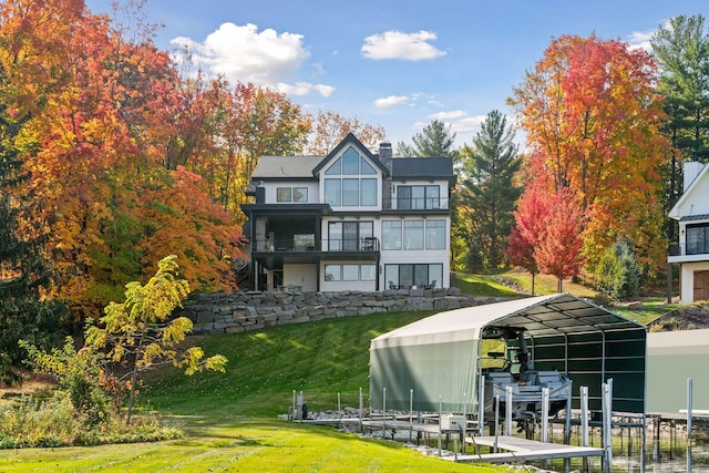 back of house featuring a yard, boat lift, a balcony, and a chimney