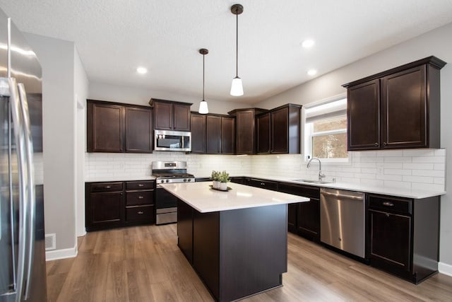 kitchen with a sink, stainless steel appliances, light wood-style floors, and decorative backsplash