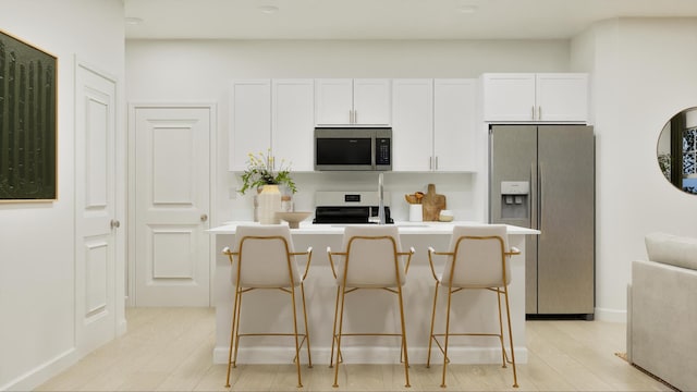 kitchen with a center island, a breakfast bar area, light wood-type flooring, appliances with stainless steel finishes, and white cabinetry