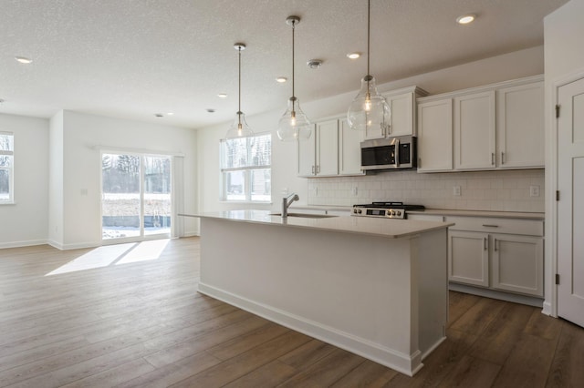 kitchen with a sink, stainless steel microwave, backsplash, dark wood finished floors, and stove