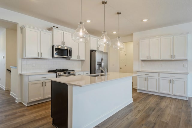 kitchen featuring dark wood-style floors, a center island with sink, a sink, stainless steel appliances, and white cabinets