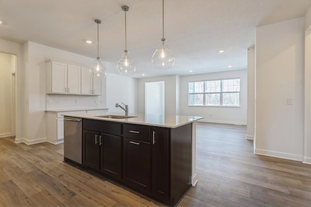 kitchen featuring wood finished floors, white cabinetry, a sink, light countertops, and stainless steel dishwasher