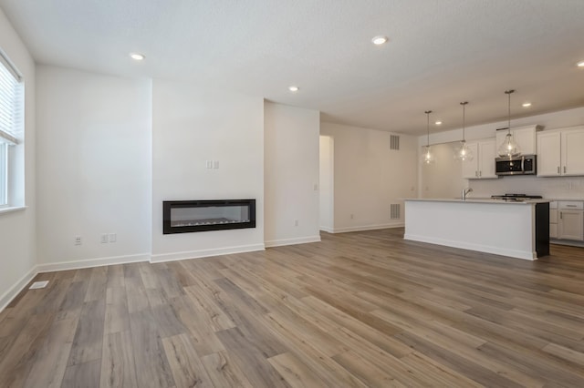 unfurnished living room featuring a glass covered fireplace, light wood-style flooring, and baseboards