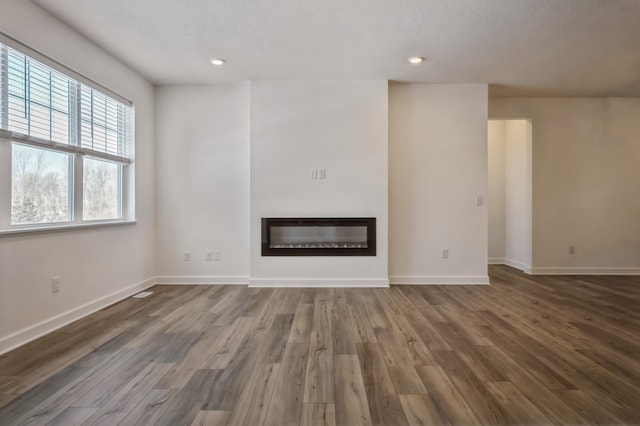 unfurnished living room with a glass covered fireplace, recessed lighting, baseboards, and wood finished floors