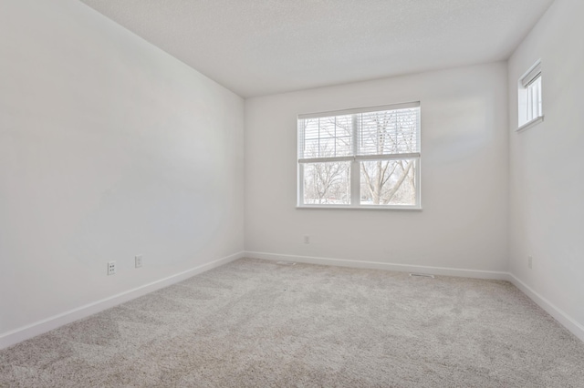 empty room featuring light carpet, a textured ceiling, and baseboards