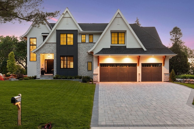 view of front of home with decorative driveway, a lawn, stone siding, and a shingled roof