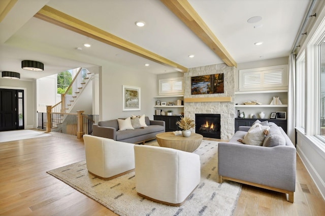 living room featuring beamed ceiling, a fireplace, wood finished floors, and stairs