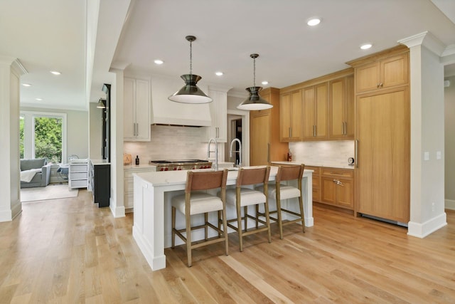 kitchen with light wood finished floors, backsplash, light countertops, a kitchen breakfast bar, and a kitchen island with sink