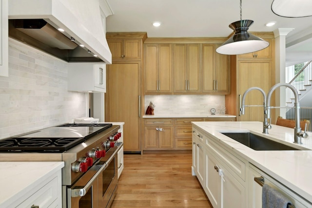 kitchen with wall chimney range hood, range with two ovens, light wood-style floors, hanging light fixtures, and a sink