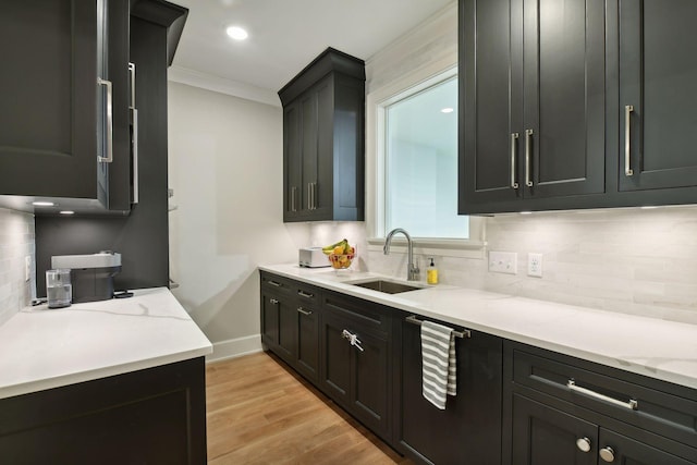 kitchen featuring a sink, backsplash, crown molding, light wood finished floors, and baseboards